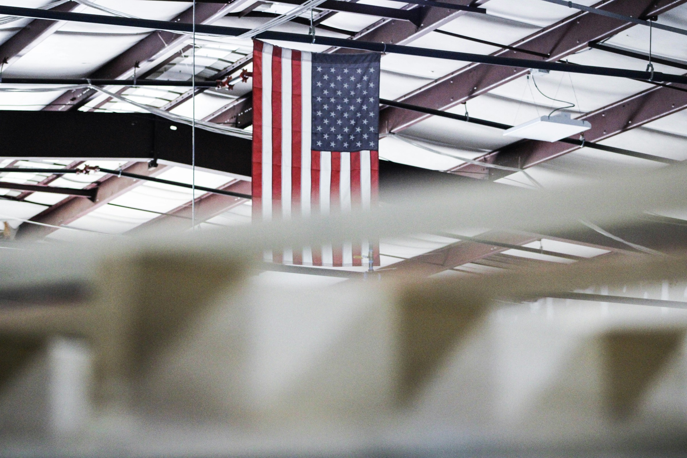 American flag hanging from the steel roof structure of a bright factory floor